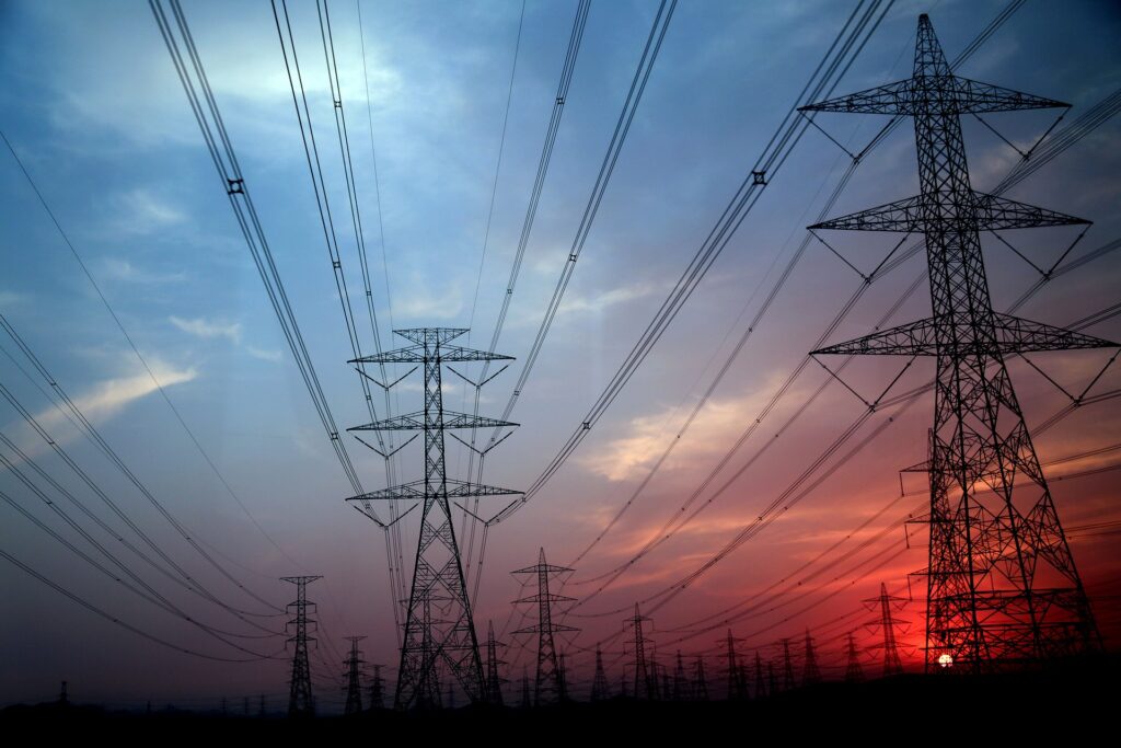 A field of electricity pylons connecting to each other in front of a sunset sky.